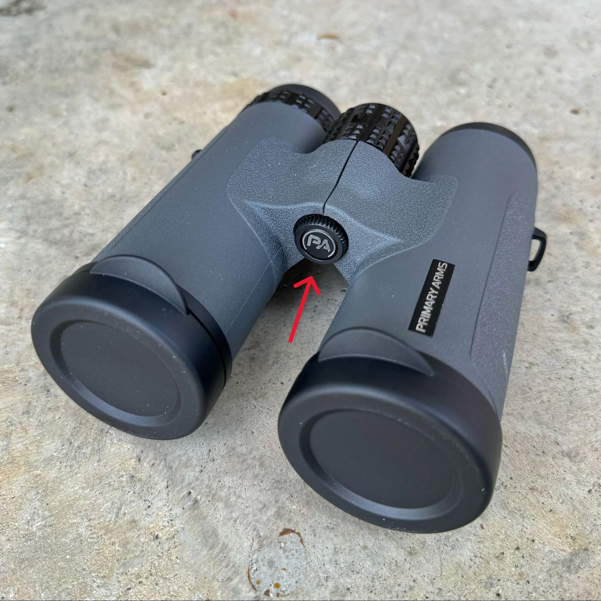 Close-up of the GLx binoculars showing the tripod adapter underneath a cap with the Primary Arms logo