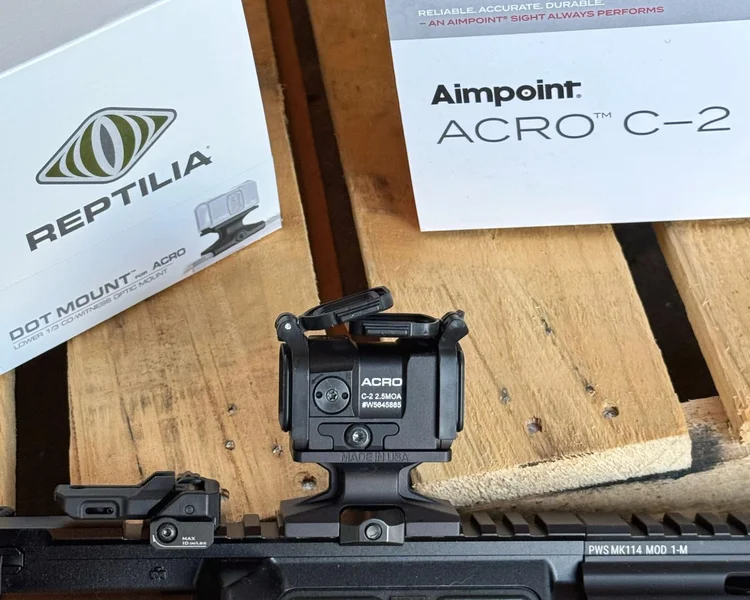 Close-up of the Aimpoint Acro C-2 optic mounted on a carbine with a new TMAG magazine nearby.