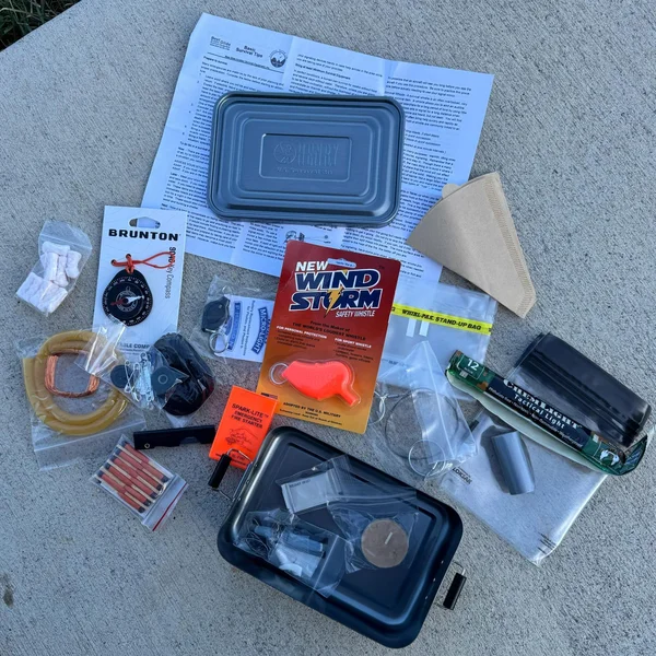 Henry Survival Kit contents including compass, fire starters, and medical supplies, spread out for display