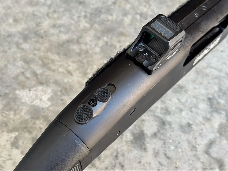 Close-up of Mossberg 590S Compact shotgun’s top-mounted ambidextrous safety and rear sight, viewed from above on a concrete surface.