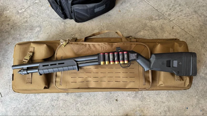Fully customized Mossberg 590S Compact shotgun with optic, Magpul stock and forend, and Esstac shell card, displayed on a tan rifle case on a concrete floor.