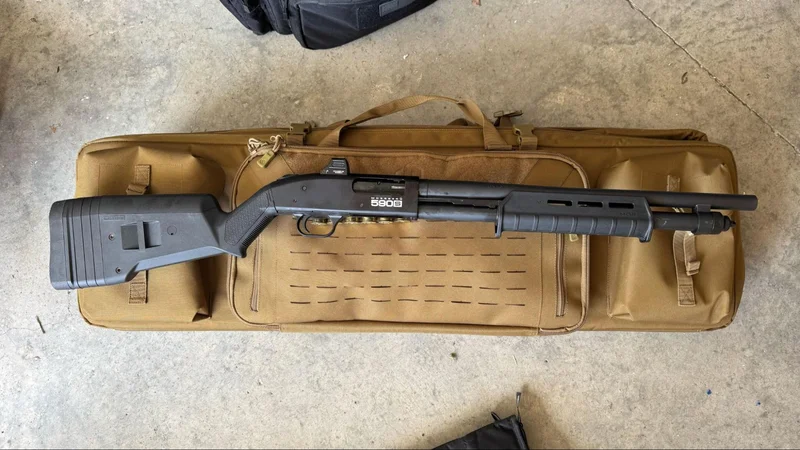 Mossberg 590S Compact Optic-Ready shotgun displayed on a tan rifle case, featuring an upgraded stock and forend, photographed indoors on a concrete floor.