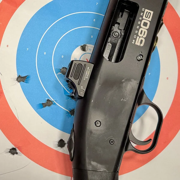 Mossberg 590S Compact receiver and trigger group resting on a paper bullseye target, showing tight shot grouping after range testing.