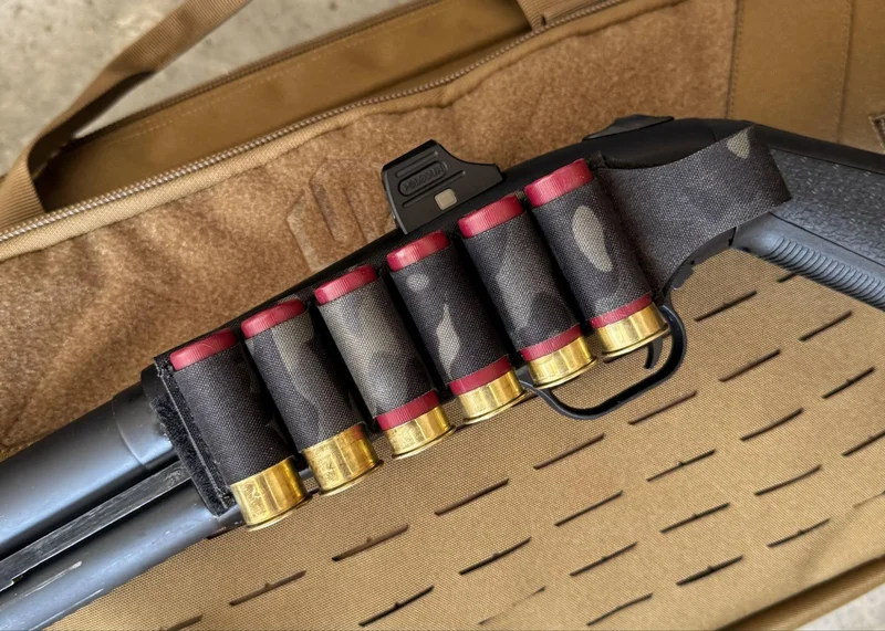 Mossberg 590S Compact shotgun with an Esstac Velcro-backed shotgun card holding six 12-gauge shells attached to the receiver, resting on a tan rifle case.