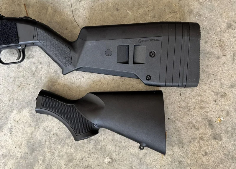 Side-by-side comparison of upgraded Magpul SGA stock installed on Mossberg 590S Compact shotgun next to the original compact factory stock on a concrete surface.