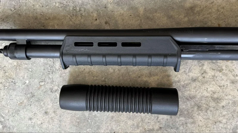 Top-down view of the Mossberg 590S Compact equipped with a Magpul MOE M-LOK forend, placed above the original factory forend on a concrete surface.