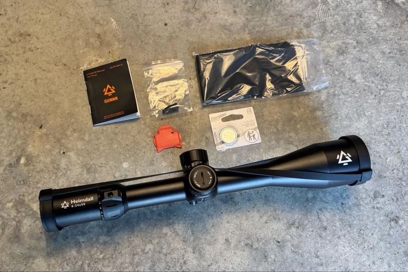 ontents of the GUNNR HEIMDALL HPVO scope package including scope, throw lever, battery, lens covers, tool, cleaning cloth, and manual