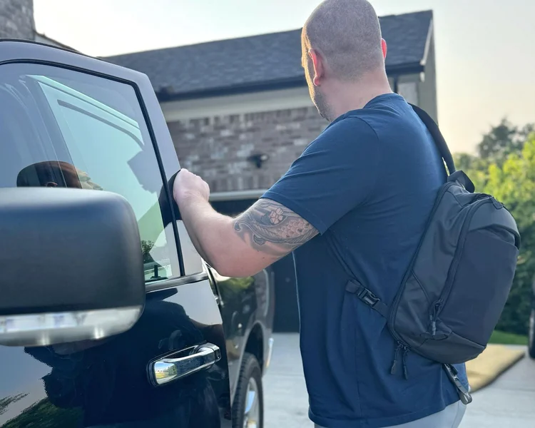Man wearing VERTX Urban Ghost Sling Bag on back while unlocking a vehicle