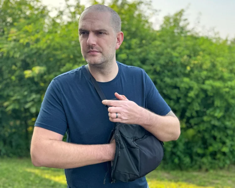 Man wearing a sling bag with hand inside the CCW compartment, demonstrating discreet access