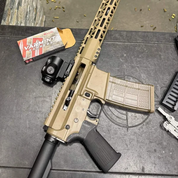 Bear Creek Arsenal BC-15 rifle with Flat Dark Earth Cerakote and black furniture on shooting bench with ammo, multitool, and red dot sight