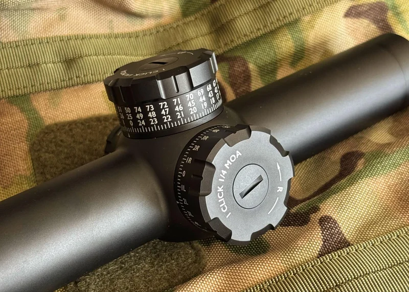Close-up of the elevation and windage turrets on the GUNNR Odin LPVO optic, showing tactile dial markings and turret cap on a camouflage background