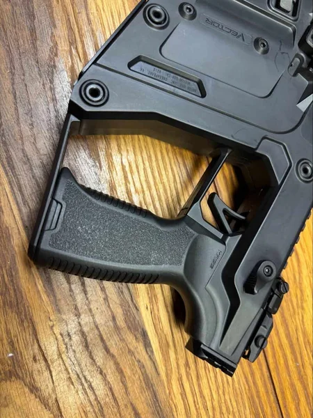 Close-up side view of Kriss Vector Gen 3 pistol grip and lower receiver on a wooden table.