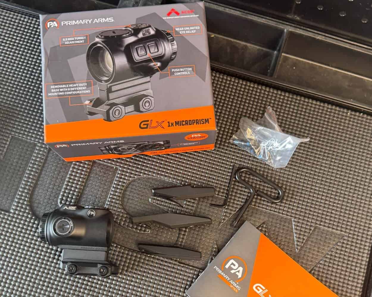 GLx 1x MicroPrism optic and accessories laid out on a mat, including the box, mount, spacers, tools, and user manual.