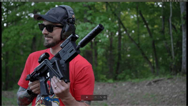 Man aiming Kriss Vector Gen 3 with folding stock and optic in an outdoor wooded area.