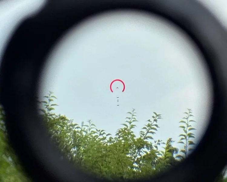 View through the GLx 1x optic showing a red reticle over green foliage outdoors.