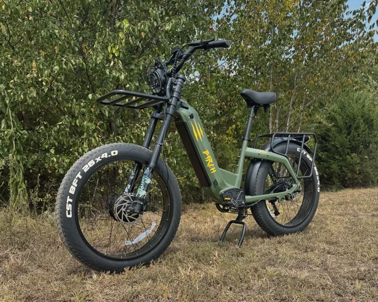 Birch Grolar AWD hunting bike in green color parked on grass with wooded background, showcasing its off-road capabilities and camouflage design.
