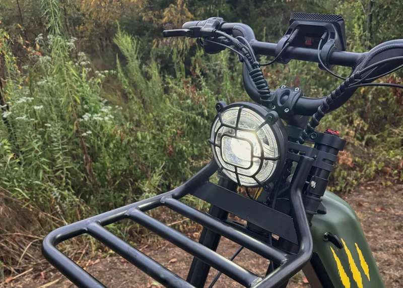 Front view of Birch Grolar AWD hunting bike showing bright LED headlight, front rack, and handlebar display in wooded terrain.