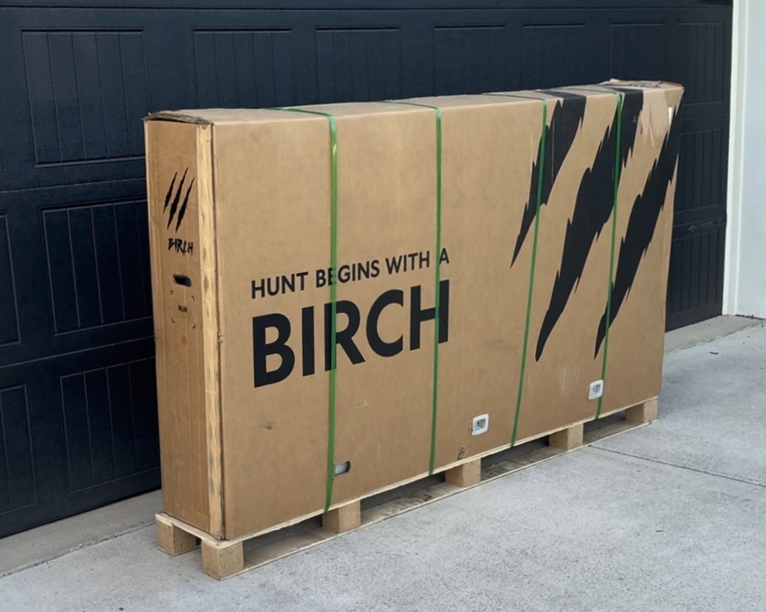 Large Birch Grolar AWD hunting bike shipping box on a pallet, delivered securely in protective packaging in front of a garage.