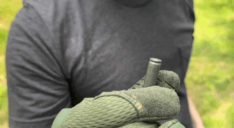 Close-up of gloved hand holding a stuck steel-case round extracted from the IWI Carmel rifle