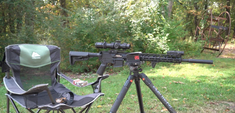 Rock River Arms LAR-15M .17 HMR rifle mounted on tripod at outdoor shooting range with ammo and chair beside it