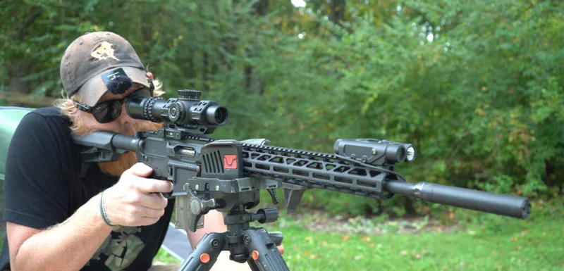Shooter testing the Rock River Arms LAR-15M .17 HMR rifle with scope and suppressor mounted on tripod