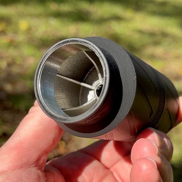 Close-up of hand holding BANISH Speed K suppressor showing internal baffles and threaded mount