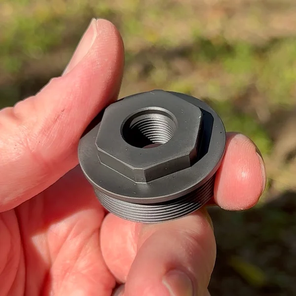 Close-up of hand holding BANISH Speed K suppressor thread mount adapter for rifle compatibility
