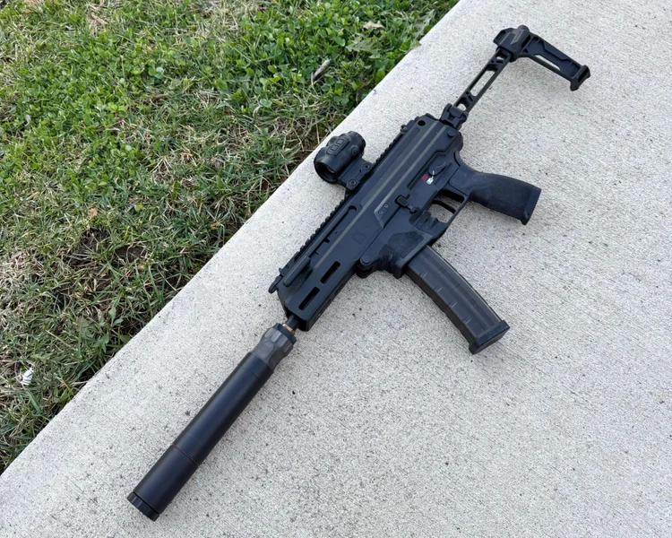 Compact firearm equipped with Silencer Central BANISH 45 suppressor resting on concrete beside grass