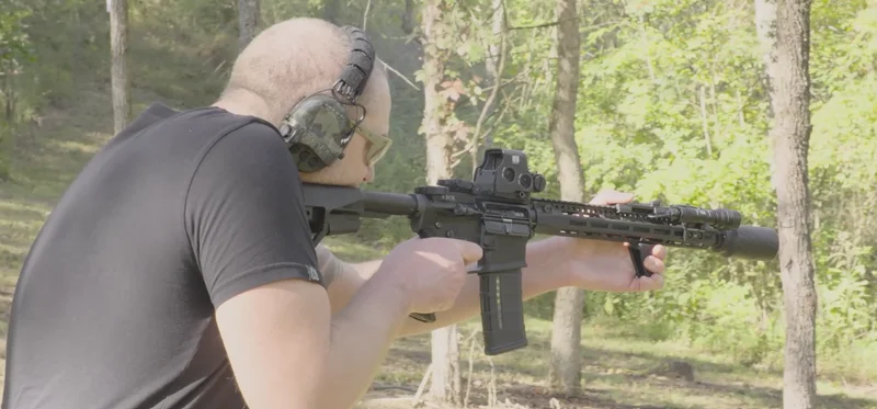 Man shooting AR-15 with BANISH Speed K suppressor in wooded outdoor range wearing ear protection