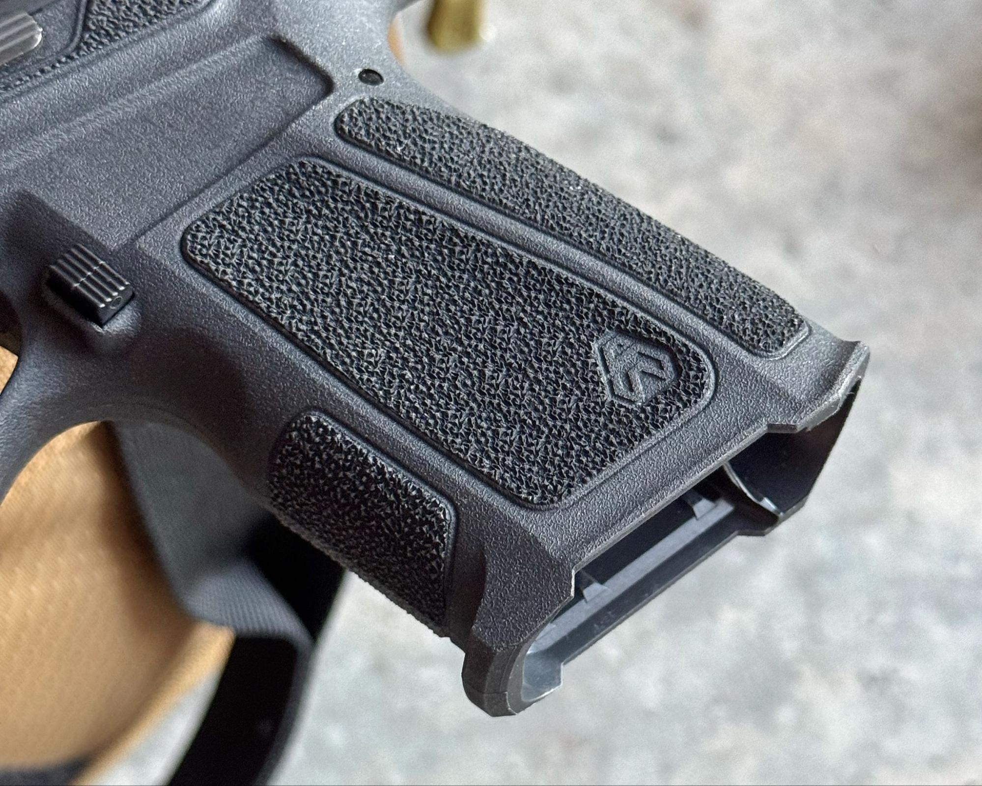 Close-up of the aggressive grip texturing and ergonomic beavertail on the Strike Arms compact pistol frame.