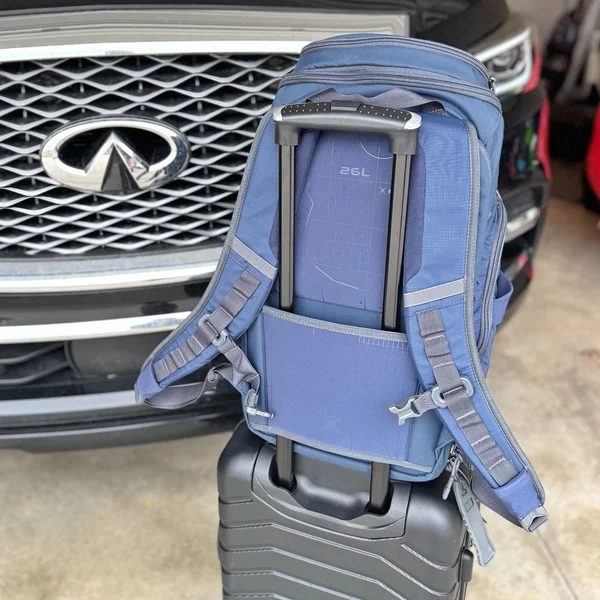 Blue Vertx Gamut 26L backpack attached to rolling luggage via its integrated pass-through