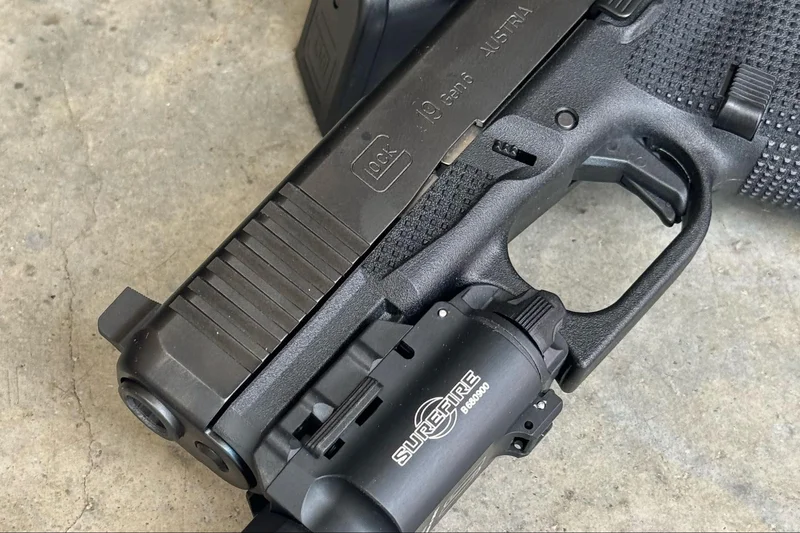 Close-up of the integrated thumb ledge molded into the Glock 19 Gen6 frame with a Surefire light attached to the rail