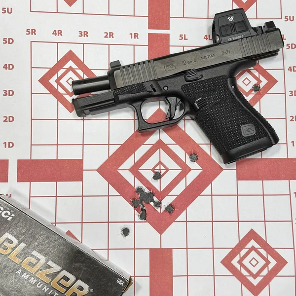 Glock 19 Gen6 with the slide locked back, positioned over a paper target showing a tight 7-yard shot grouping