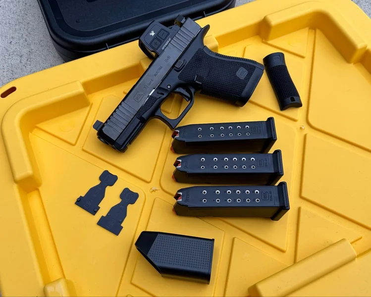 Overhead view of the Glock 19 Gen6 unboxed with three 15-round magazines, interchangeable backstraps, optic plates, and a magazine loader