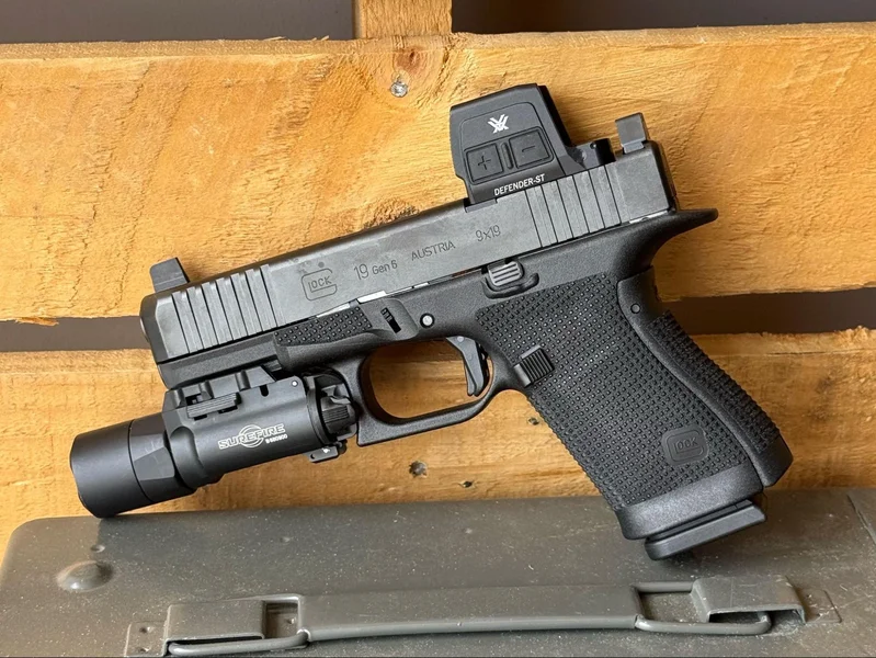 Side profile of the Glock 19 Gen6 featuring a Vortex Defender-ST optic and Surefire weapon light resting on a metal ammo can