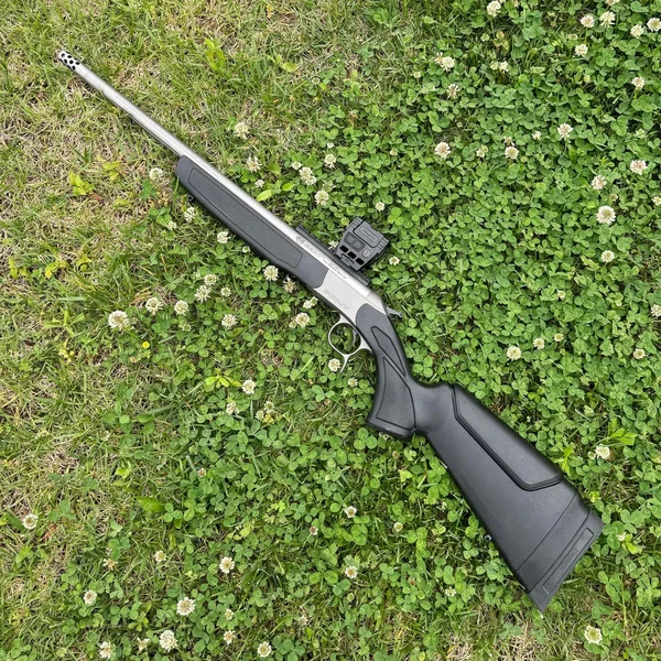 CVA Scout TD single-shot rifle in .223 Remington equipped with a Holosun AEMS red dot optic on a grass background.