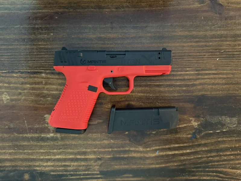 Mantis TitanX laser pistol and a single training magazine displayed on a wooden surface, highlighting the dedicated training platform