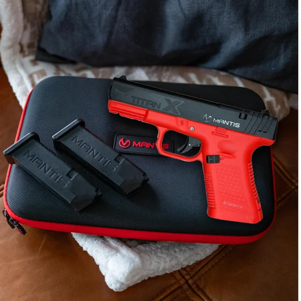 Mantis TitanX training pistol resting on its dedicated red-and-black hardshell carrying case with two training magazines