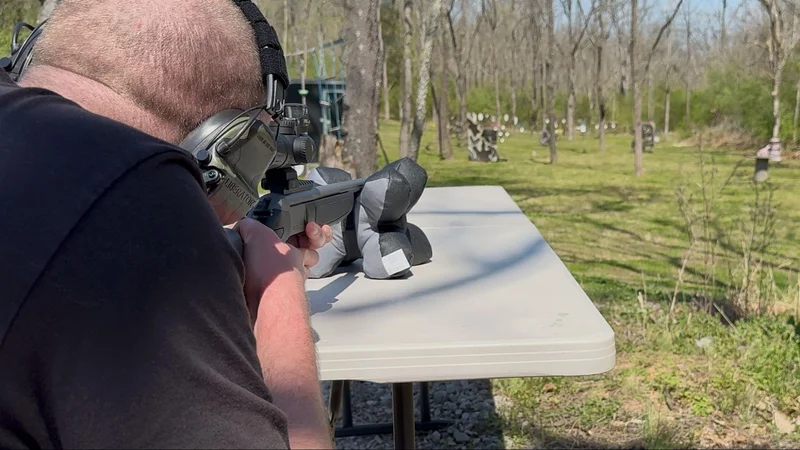 Over-the-shoulder view of a shooter aiming a CVA Scout TD with an Eotech Vudu scope at distant steel targets